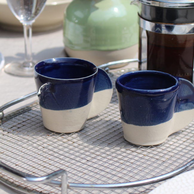 Cette tasse à café dégage un charme rustique et authentique grâce à son émail artisanal et à son design simple mais efficace. Le contraste entre le bleu nuit et la terre brut renforce la brillance de l'émaille.