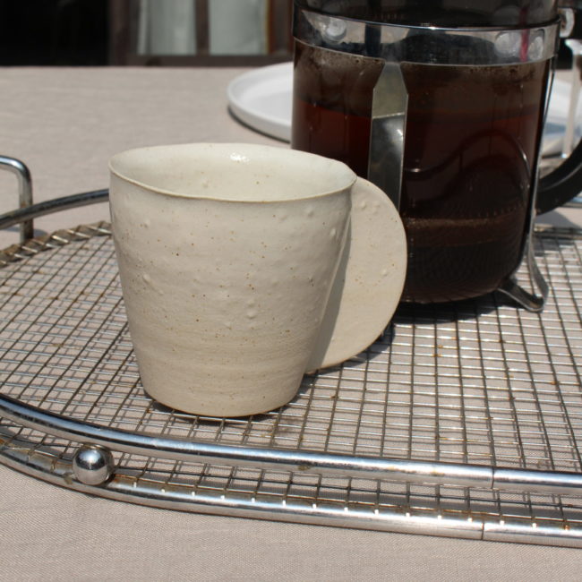 Cette tasse à café blanche dégage un charme rustique et authentique grâce à son émail artisanal et à son design simple mais efficace.