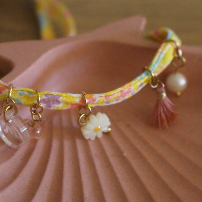 Bracelet biais en tissus de couleurs jaune avec fleurs turquoise et Lila. Décoration de plusieurs breloques style pompons et perles