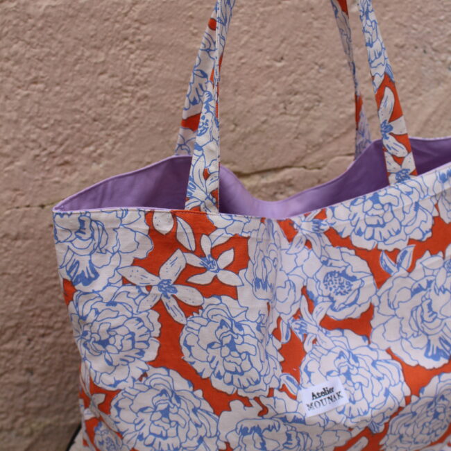 Ce sac cabas a fleurs est un incontournable pour un look décontracté. Fleurs bleues sur fond orange. Offrant une grande capacité de rangement.